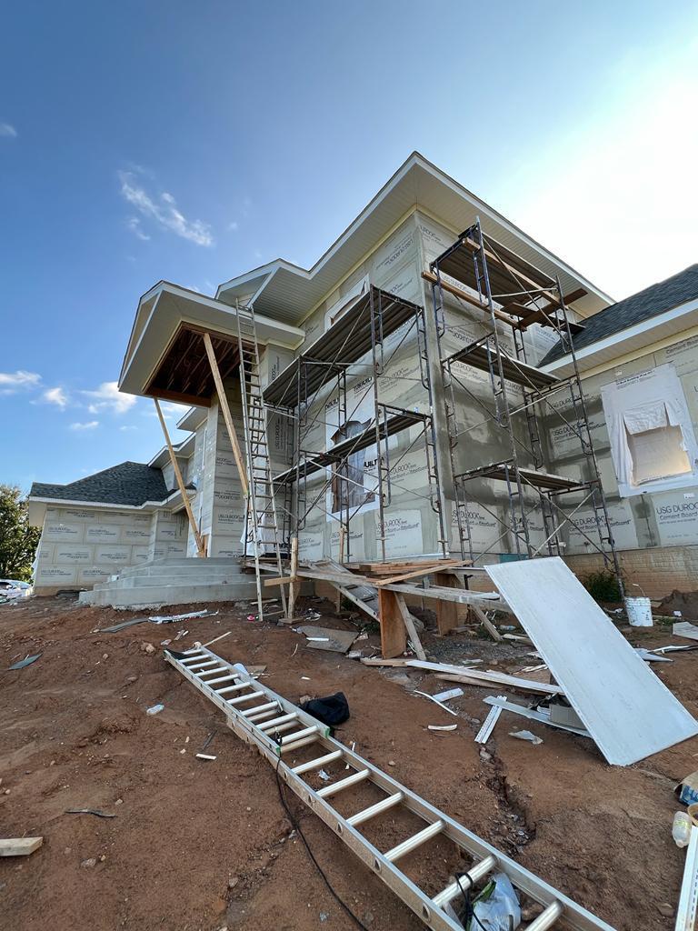 Scaffolding set up along the side of a building under construction, with a ladder and construction materials on the ground.