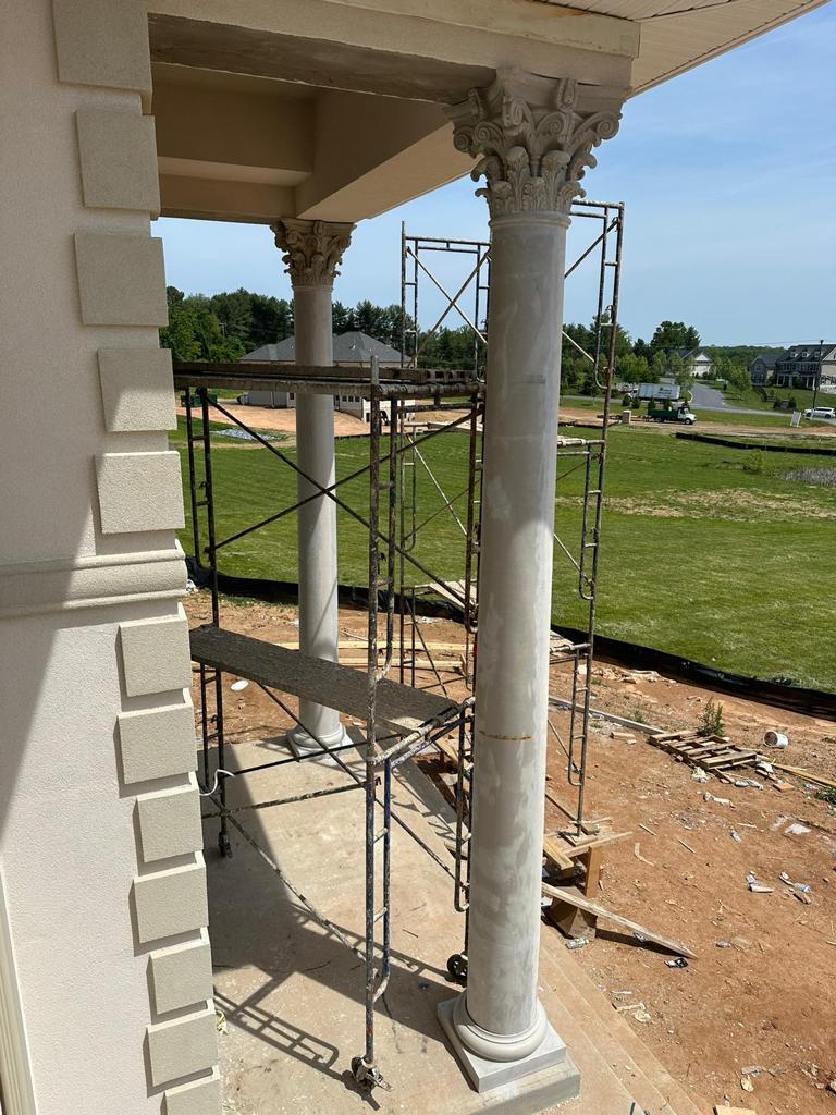 Scaffolding around large columns in front of a building, with grass and dirt in the background.