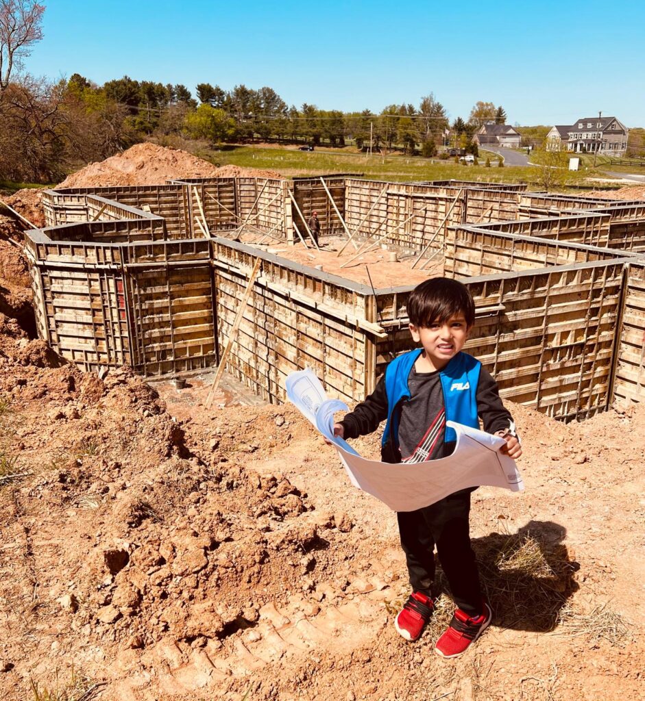 A young child holding a blueprint, standing in front of a construction site with metal framework in the background.