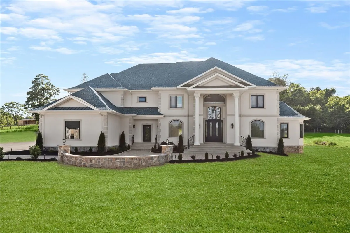 A striking two-story home featuring a grand entry with pillars, black iron doors, and a well-manicured lawn, surrounded by lush greenery.