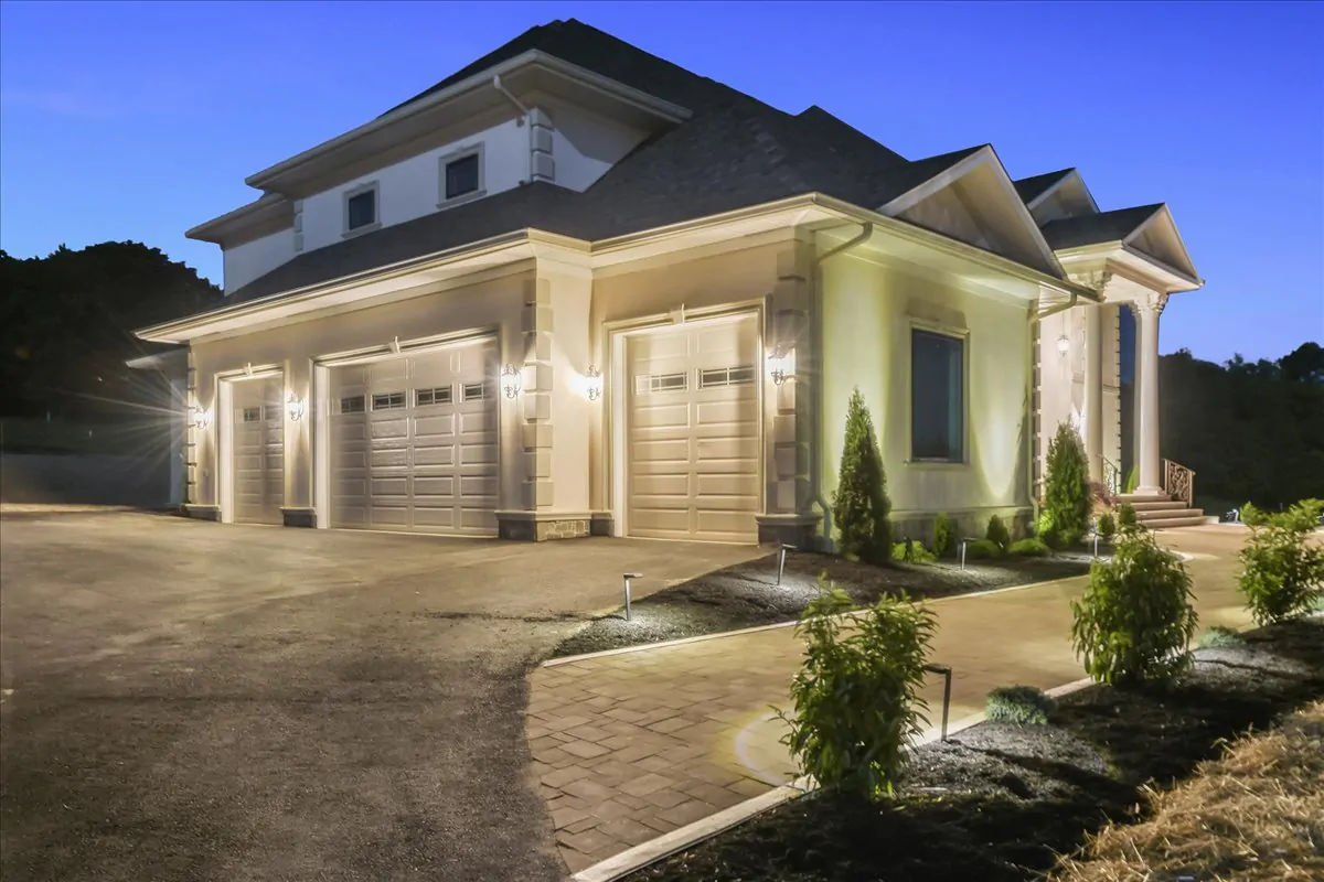 A large luxury home with a three-car garage, beautifully illuminated in the evening, showcasing the home’s grand design.