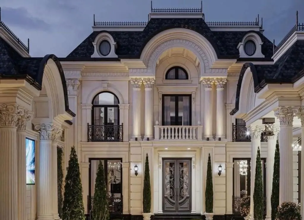 An extravagant mansion illuminated at night, with intricate architectural details and tall pillars framing the front entry